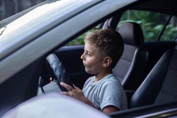 Little boy sitting in front of the car holding steering wheel