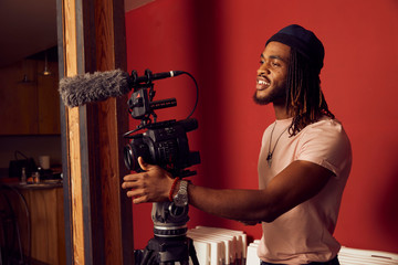 Portrait of a young ethnic man standing on a film set running motion camera on a tripod with microphone 