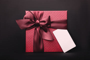 A beautiful red gift box with an empty tag on the black background. Copy Space.