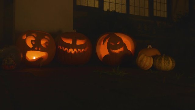 3 carved lit pumpkins outside the front of a house halloween with smoke and small pumpkins
