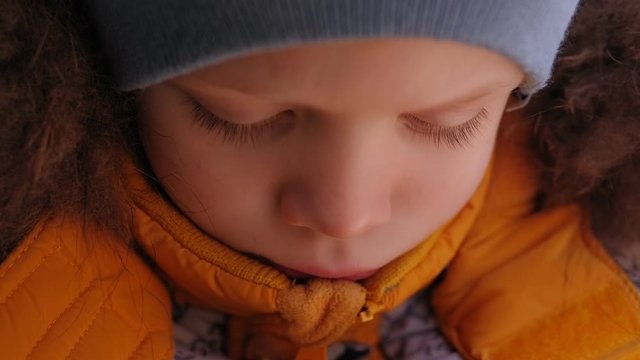 Close-up of the face of a sad little boy in a yellow winter jacket with a hood with fur in the car in the back seat in the car seat. Slow motion.