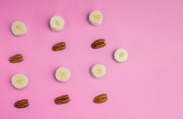 Elements to make a smoothie, banana slices and pieces of walnuts on a lilac background
