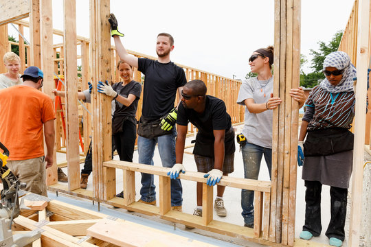 Volunteers holding framed wall at construction site