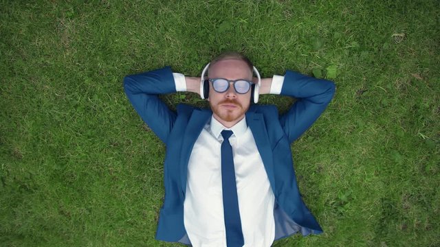 Top view of Young Businessman Lying On Grass Enjoying Music On Headphones In Park