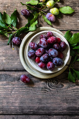 Ripe juicy plums in a bowl on a wooden background. Top view flat lay. Copy space.