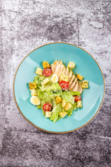 Fresh Caesar salad with grilled chicken, romaine salad leaf, cherry tomato, quail eggs and parmesan cheese on gray background copy space. Top view. Flat lay