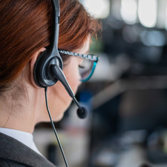 Rear view of a female helpdesk operator. An office manager with a headset answers customer calls....