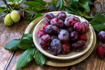 Ripe juicy plums in a bowl on a wooden background.