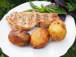 Golden-crusted potatoes with pork steak with a Basil leaf on a plate. the food is cooked on the grill.