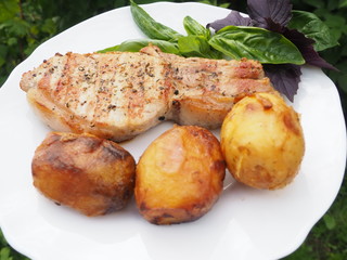 Golden-crusted potatoes with pork steak with a Basil leaf on a plate. the food is cooked on the grill.