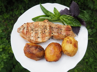Golden-crusted potatoes with pork steak with a Basil leaf on a plate. the food is cooked on the grill.