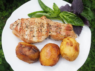 Golden-crusted potatoes with pork steak with a Basil leaf on a plate. the food is cooked on the grill.