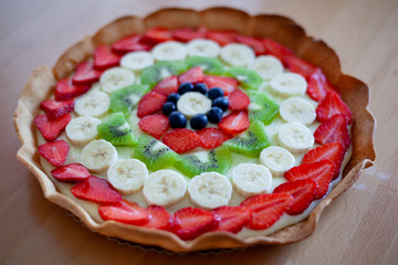 Crostata di frutta fatta in casa con fragole, mirtilli, kiwi, banane e crema pasticciera. Focus su dettagli, colori, dimensioni e fondo di biscotto.