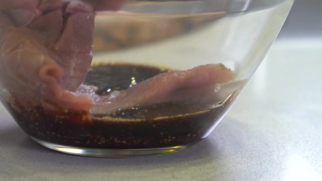 Chef placing meat in glass bowl for marination, close up