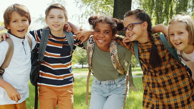 Group of happy multiethnic schoolchildren of elementary age hugging, looking at camera and smiling while posing together in the park