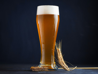 A glass of unfiltered foamy beer on a dark table