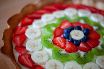Crostata di frutta fatta in casa con fragole, mirtilli, kiwi, banane e crema pasticciera. Focus su dettagli, colori, dimensioni e fondo di biscotto.
