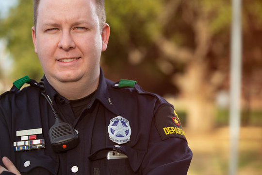 Portrait of Police officer standing outside with arms crossed looking towards camera smiling 