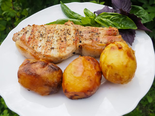 Golden-crusted potatoes with pork steak with a Basil leaf on a plate. the food is cooked on the grill.