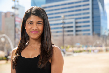 Smiling portrait of young ethnic woman standing in park wearing black tank top 
