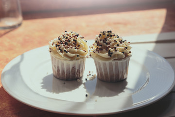 Appetizing cupcakes with white cream decorated with balls of confectionery powder lit by the rays of the sun.