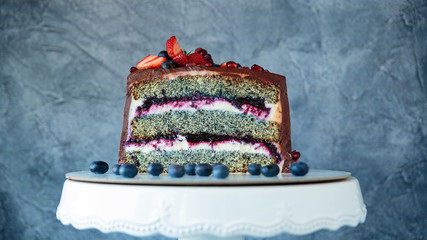 Appetizing chocolate cake decorated with strawberries, blueberries and a pomegranate sectional view with poppy seed filling on gray background.