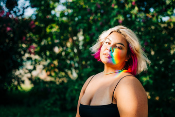 Plus size woman with rainbow lights falling on her face in park
