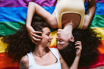 Romantic lesbian couple looking at each other while lying on rainbow flag