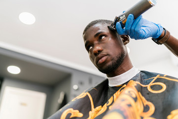 Male hairdresser wearing glove cutting young man's hair with razor in barber shop