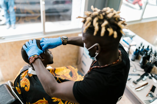 Hairdresser with locs cutting male customer's hair in barber shop
