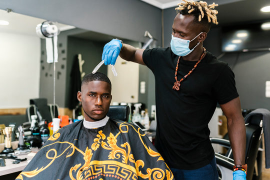 Male hairdresser wearing salon and gloves cutting young man's hair in barber shop