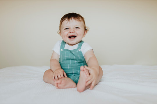 Cute baby girl laughing while sitting on bed against wall at home