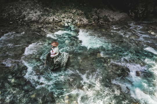 European yamabushi monk sitting on rock in the middle of river and meditating