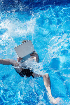 Young man with laptop falling in swimming pool during sunny day