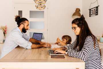 Woman working over laptop while father and daughter painting on dining table at home