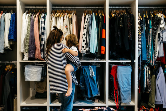 Mother carrying daughter while choosing clothes in dressing room at home