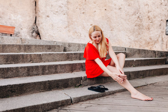 Woman wearing red dress sitting on steps and massaging her foot