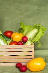 Fruits and veggies in wood box with green background.