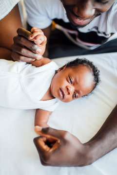 Close-up Of Parents Holding Newborn Daughter's Hands Lying On Bed At Home