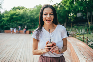 Cheerful young woman holding soft drink cup while standing in park