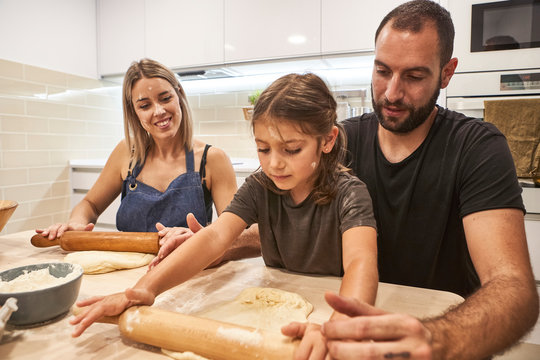 Family kneading pizza dough with rolling pins on table in kitchen