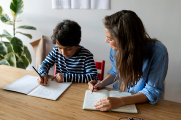 Young woman sitting with student doing homework on table at home