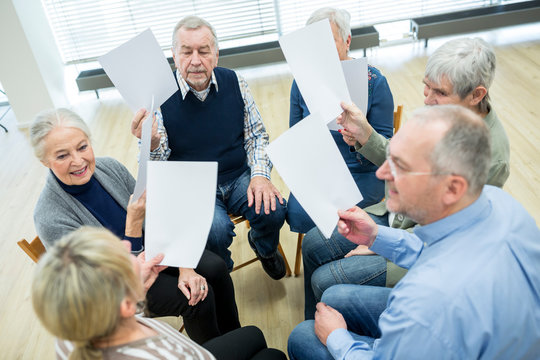 Group of seniors attending therapy group in retirement home, using sheets of paper