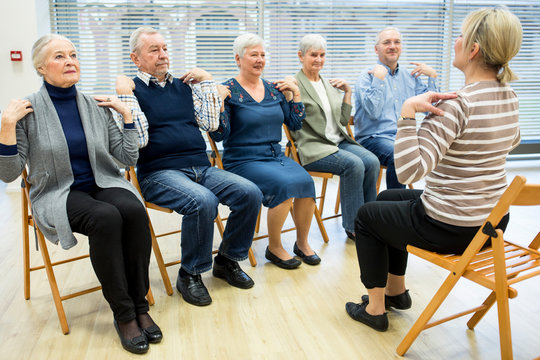 Group of seniors practicing chair gymnastics with instructor  in retirement home