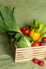 Fruits and veggies in wood box with green background.