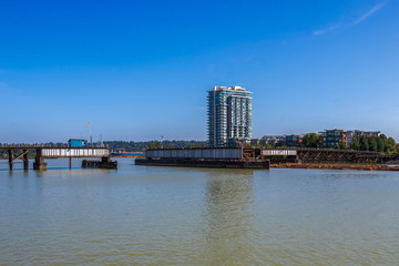 Fototapeta premium Most kolejowy nad rzeką Fraser obok dzielnicy mieszkalnej New Westminster City na tle błękitnego nieba