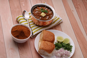 Pav Bhaji, it is Thick and spicy vegetable curry and served with a soft bread and butter. With pavbhaji masala on wooden background.