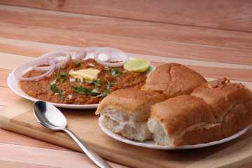 Pav Bhaji is a fast food dish from India, Thick and spicy vegetable curry, fried and served with a soft bread roll/Bun Paav and butter. Served over colourful or wooden background