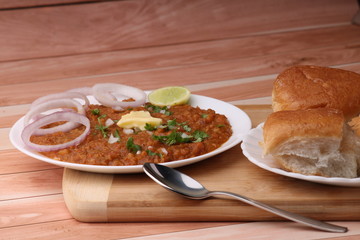 Pav Bhaji is a fast food dish from India, Thick and spicy vegetable curry, fried and served with a soft bread roll/Bun Paav and butter. Served over colourful or wooden background