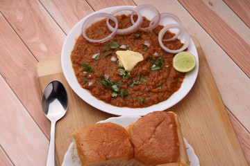 Pav Bhaji is a fast food dish from India, Thick and spicy vegetable curry, fried and served with a soft bread roll/Bun Paav and butter. Served over colourful or wooden background
